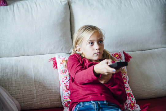 Young Girl Changing Channel With Remote Control In Front Of Television At Home