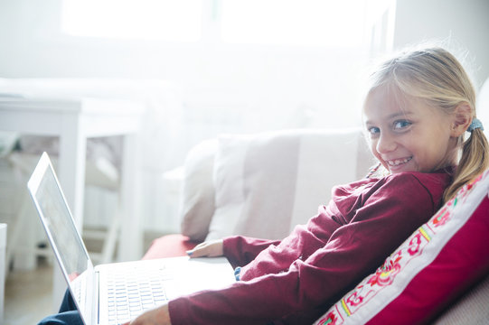Happy  little girl lying on the sofa with laptop in the living room at home.