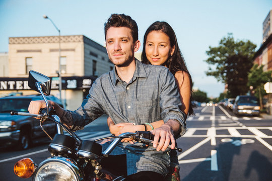 A young woman holds onto a man while they ride a motorcycle in the city