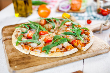 hot fresh homemade traditional italian pizza with cheese, tomatoes and rocked salad on wooden cooking table. wallpaper for pizzeria and food concept