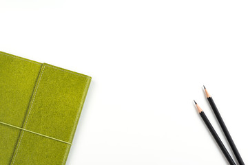 Recycled paper notebook in green colour and two black pencils over white background with copy space for text insertion, green concept environment for saving earth