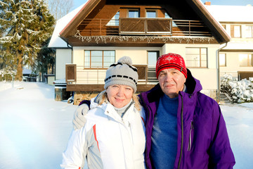 Portrait of cute happy middle aged couple husband wife winter snow outdoors near the house.