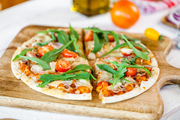 hot fresh homemade traditional italian pizza with cheese, tomatoes and rocked salad on wooden cooking table. wallpaper for pizzeria and food concept