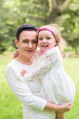 Naklejka premium family, children and happy people concept - happy little girl hugging her mother over green background