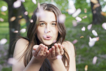 Beautiful girl blowing a handful of flowers, outdoors, in a spring park.