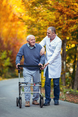 Male nurse assisting senior patient with walker outdoor