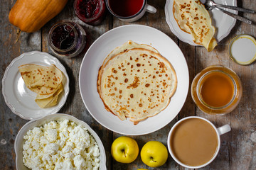 Pancakes and serving on a wooden table (honey, jam, tea, coffee, cappuccino, cocoa, cottage cheese, apples, pumpkin, etc.)