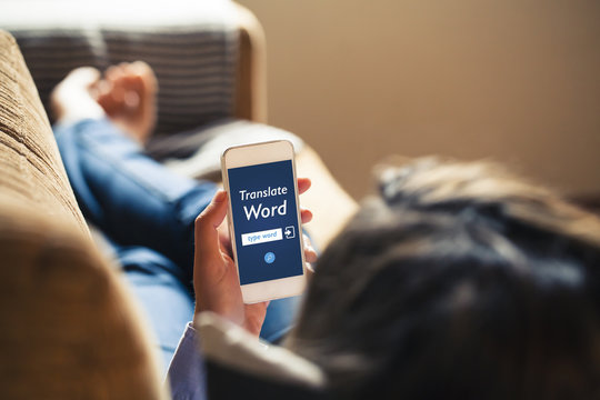 Woman Using A Mobile Phone To Translate A Word While Rest On A Couch At Home.