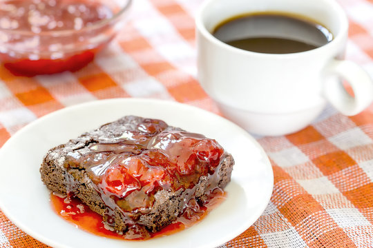 Homemade brownie covered in strawberry jam with a cup of coffee