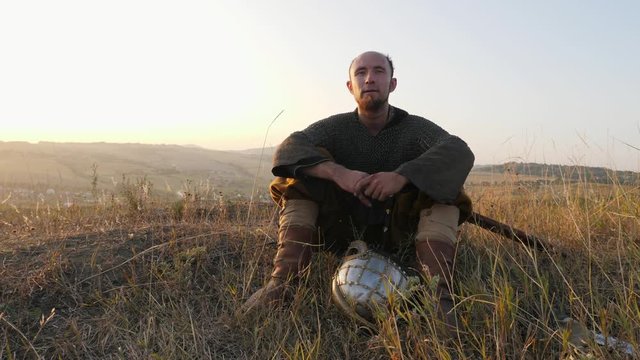 Portrait of a Viking sitting on the grass dressed in chainmail with a helmet