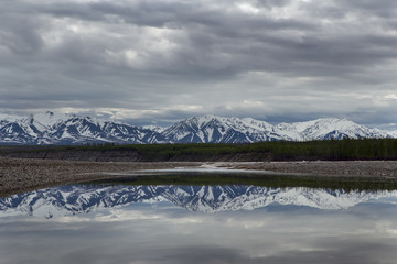 Spring mountains with remnants of snow and the reflection in the river. The River Indigirka....