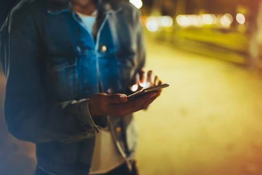 Woman pointing finger on screen smartphone on background illumination bokeh light in night city, hipster using in hands mobile phone closeup, mockup glitter street, online wifi internet concept