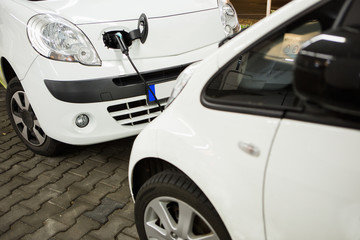 Fototapeta premium Electric car charged on a charging station in a indoor parking of shopping center by night. 