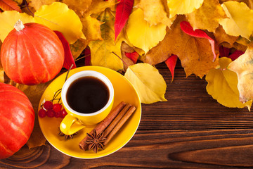 Autumn horizontal banner with yellow, red leaves, pumpkins, cup of coffee and guelder rose on brown wooden background.