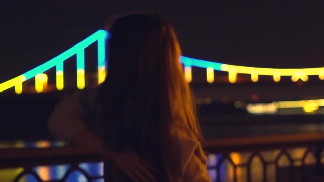 Slow motion. a young blonde girl with long curly hair dances in the night gown on the background of glowing fanfare. bright night illumination and a luminous bridge. The professional dancer moves
