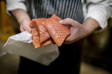 Close up of a fish monger’s hands holding three fillets of fresh filleted salmon on a market...