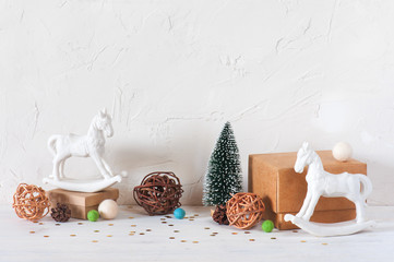 Light background with gift boxes, toy horses and small Christmas tree