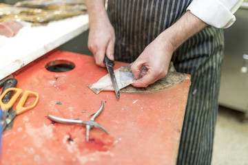 British fish monger fillets a dover sole and pulls it’s skin away on a market stall in Yorkshire,...