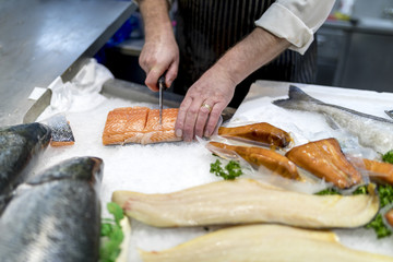 British fish monger slicing, filleting or cutting fresh slamon on ice on a market staff in...