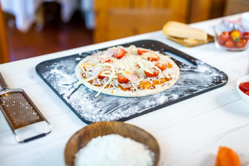 raw fresh homemade traditional italian pizza with tomatoes, cheese and han on wooden cooking table with ingredients. wallpaper for pizzeria and food concept