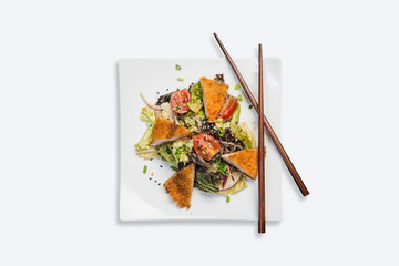 Pan-Asian salad, vegetables with fried chicken. On a square white plate with chopsticks on a white background. Top view
