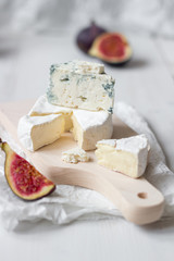 Sliced fresh camembert cheese and blue cheese with figs on the white wooden table.
