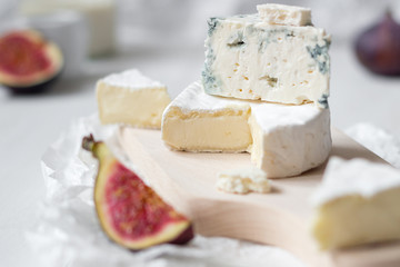 Sliced fresh camembert cheese and blue cheese with figs on the white wooden table.
