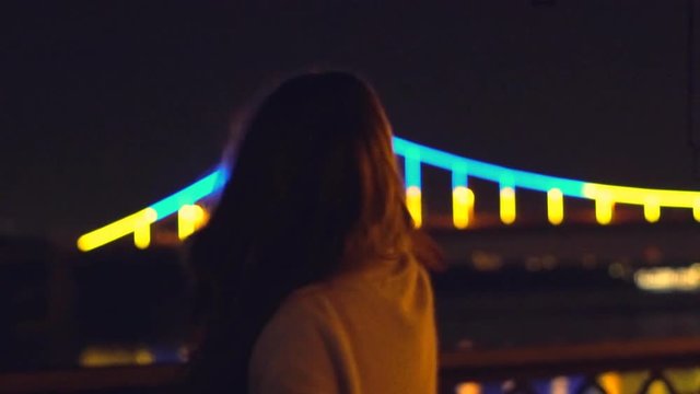 Slow motion. a young blonde girl with long curly hair dances in the night gown on the background of glowing fanfare. bright night illumination and a luminous bridge. The professional dancer moves