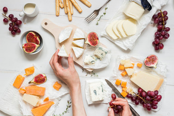 Various types of cheese with fruits and snacks on the wooden white table. Top view