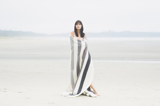 A woman wrapped in a blanket standing on a desolate beach