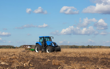 a large blue tractor, plowing field against the beautiful sky. Work of agricultural machinery. Harvest