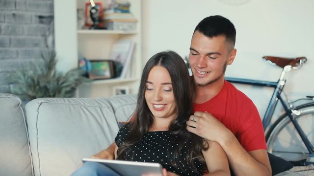couple laughing feel happy use tablet computer on the couch home watch film modern design rest together man woman attractive boyfriend girlfriend leisure love resting relationship hugging Slow motion