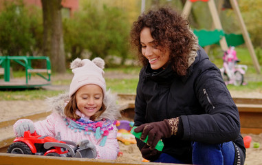 Mother playing with her daughter in a sandbox