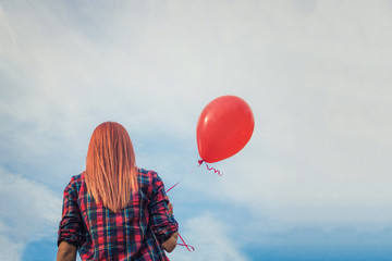Redhead girl with red balloon against the sky.
