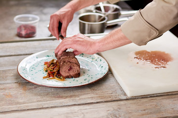 Chef putting beef meat on plate. Delicious dinner on wooden table. Veal grilled meat and vegetables.