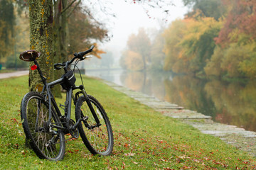 Bicycle standing near river in colorful autumn park. Fall season background.