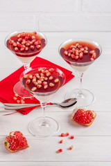 Creamy vanilla panna cotta with red jelly in beautiful glasses, fresh ripe pomegranate on white wooden background.