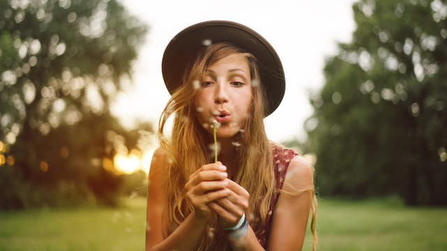 Young woman with hat blowing dandelion.