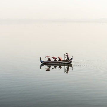 Buddhist monks in rowing boat during sightseeing tour at U- Bein bridge