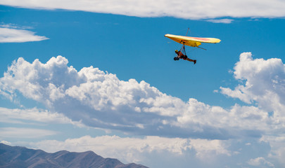Fototapeta na wymiar Orange and yellow hang glider in blue sky with clouds
