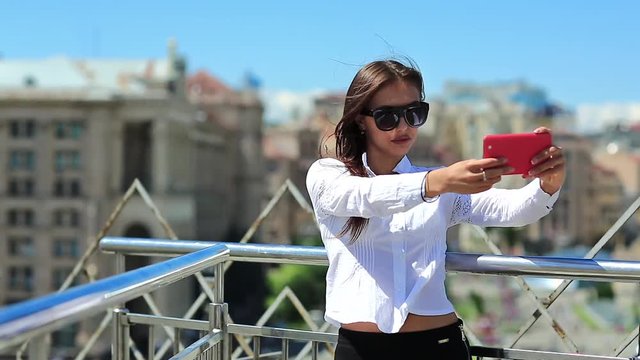 Attractive girl in sunglasses with red cell phone. Businesswoman makes selfie on his smartphone. Woman makes photos on mobile phone