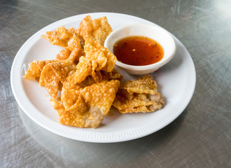 Thai style deep-fried pork dumpling serving with spicy plum sauce on white plate isolated on silver stainless steel table for crispy appetizer