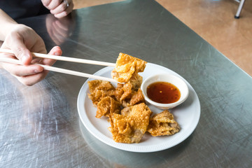 Hand holding Thai style deep-fried pork dumpling with wooden chopsticks over the dish