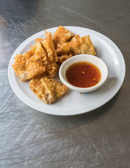 Thai style deep-fried pork dumpling serving with spicy plum sauce on white plate isolated on silver stainless steel table for crispy appetizer