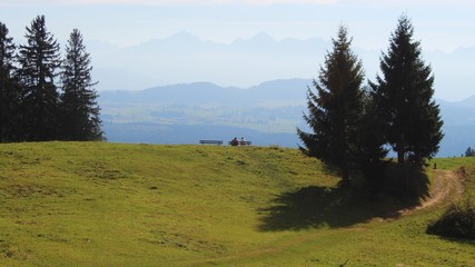Fototapeta na wymiar Glückliches Paar sitzt auf einer Bank und genießt den herrlichen Panoramablick auf die Berge, Allgäu