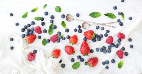 Berry frame with copy space on right. Strawberries, raspberries, blueberries and mint leaves, white wooden background, top view