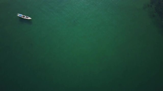 Starting out over the water, the camera looks straight down to reveal a fishing boat at anchor and then an island paradise with palm trees, white sand beach, and backpacker accommodation.