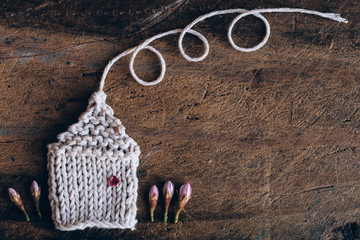 Knitted house with a smoking chimney and flowers on wooden background