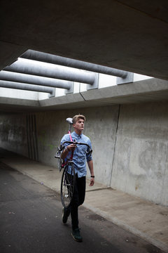 Young man walking with vintage bicycle on his shoulder in an urban bike  tunnel