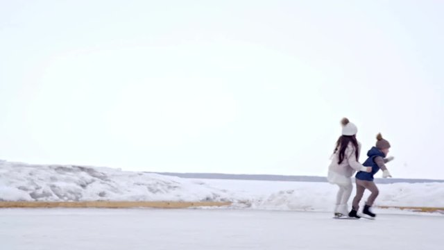 Tracking of adorable little girl in pink coat holding waist of her cute brother and ice skating on outdoor rink in winter
